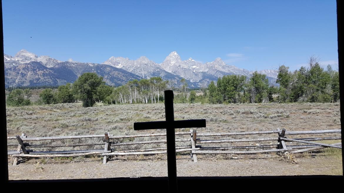 A view of the mountains from inside a cabin at Grand Teton National Park. A cross is on the window sill.